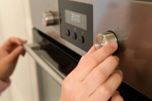 Person setting temperature on a stainless steel oven dial.