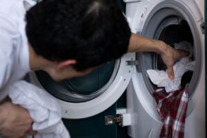 Person placing white and plaid laundry into a front-load washing machine drum.